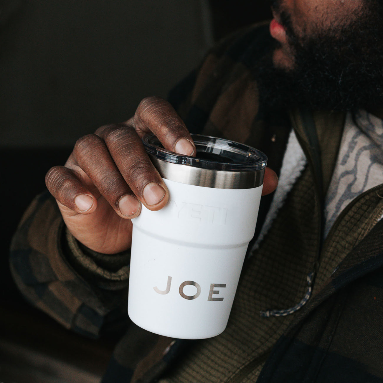 Person holding a white Yeti stackable cup, personalised with the name Joe, with a dark background