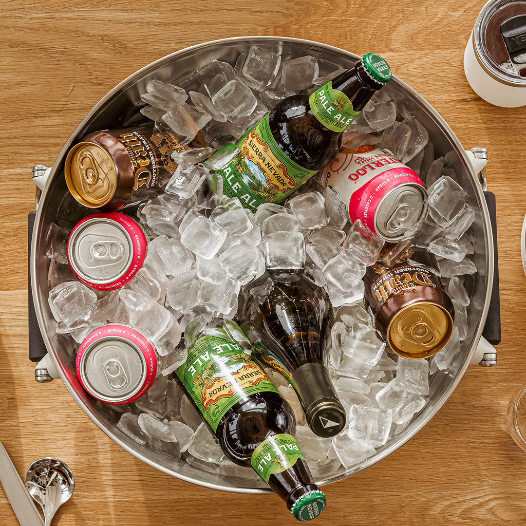 Assorted bottles and cans on ice in a beverage tub on a wooden table.