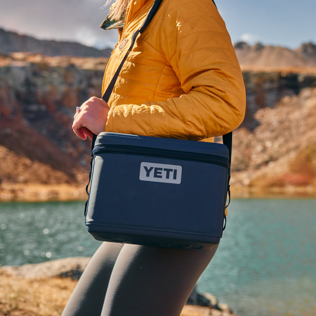 Person holding a YETI cooler by a lake with mountains in the background