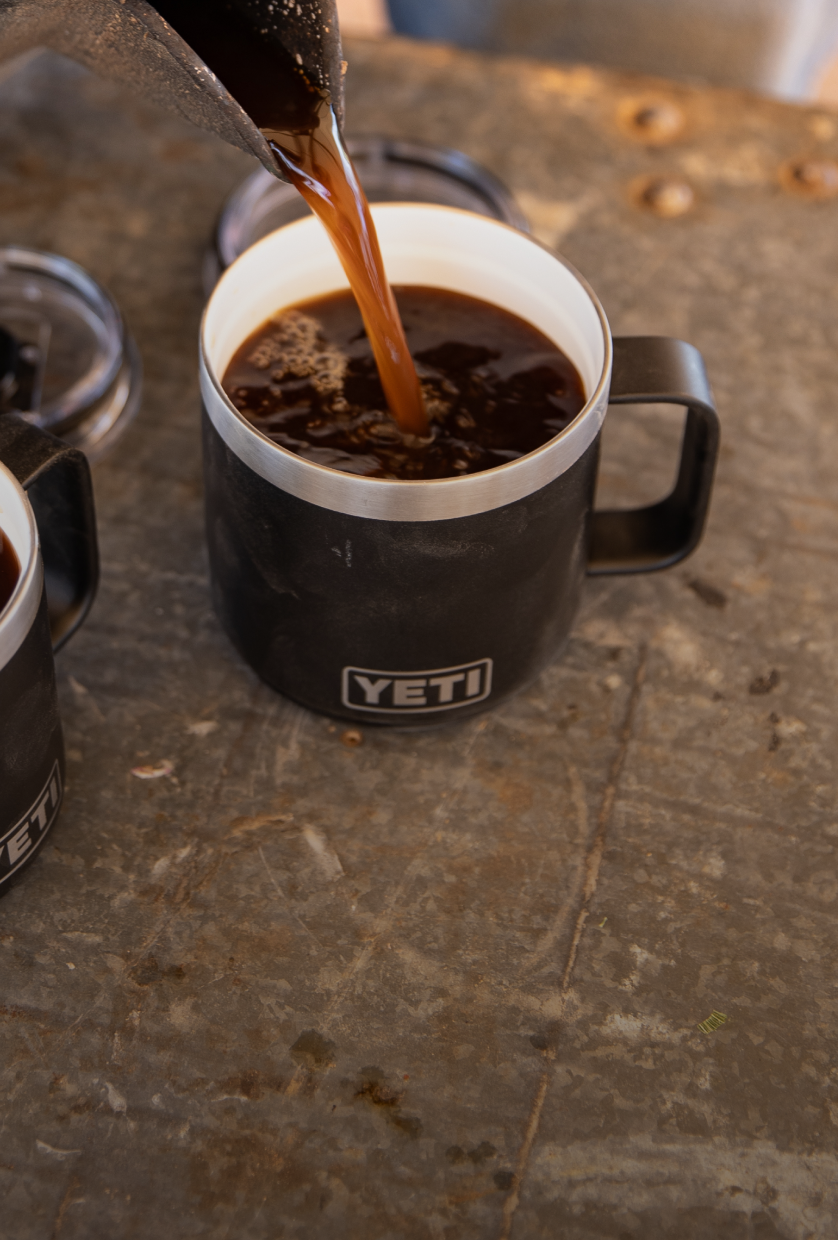 Coffee being poured into a YETI mug on a textured surface